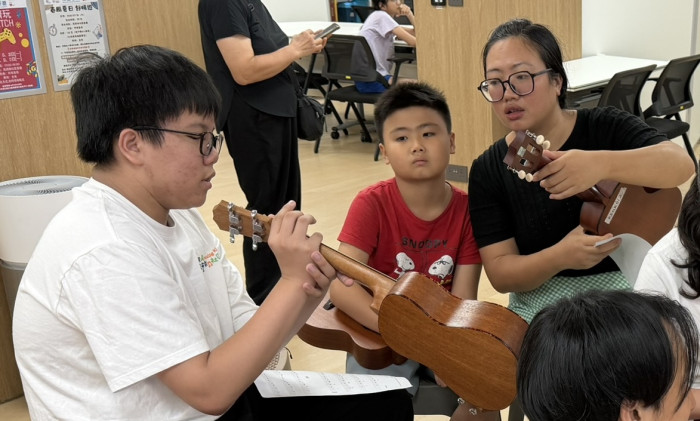 德賢在土瓜灣馬頭角社區客廳中，協助結他班導師教導土瓜灣街坊彈奏夏威夷小結他。